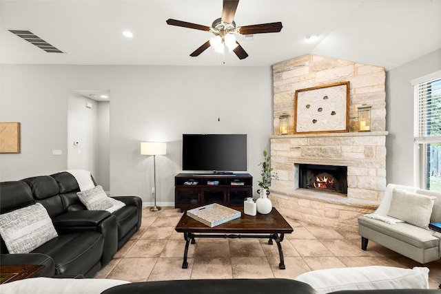 living room with baseboards, visible vents, lofted ceiling, ceiling fan, and a stone fireplace