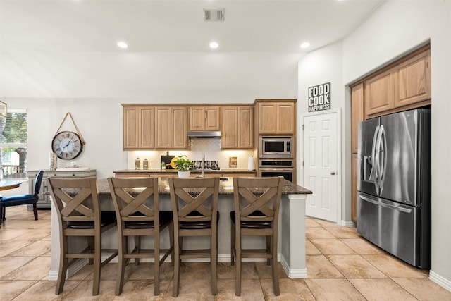 kitchen featuring visible vents, an island with sink, decorative backsplash, under cabinet range hood, and appliances with stainless steel finishes