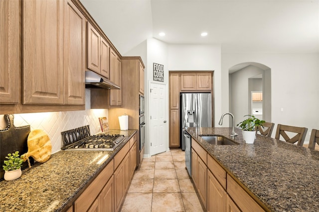 kitchen featuring arched walkways, a sink, appliances with stainless steel finishes, under cabinet range hood, and tasteful backsplash