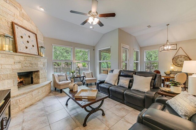 living room with lofted ceiling, ceiling fan with notable chandelier, a stone fireplace, and plenty of natural light
