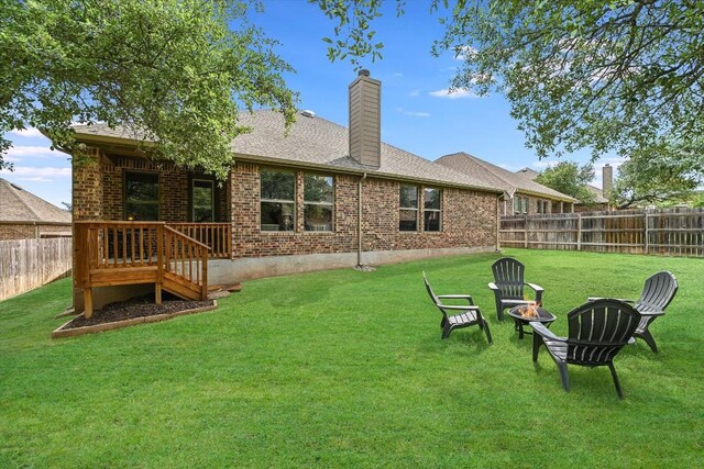 rear view of house with an outdoor fire pit, a yard, a chimney, a fenced backyard, and brick siding