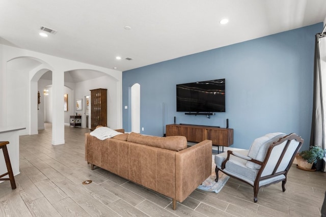 living room with arched walkways, visible vents, recessed lighting, and wood finish floors