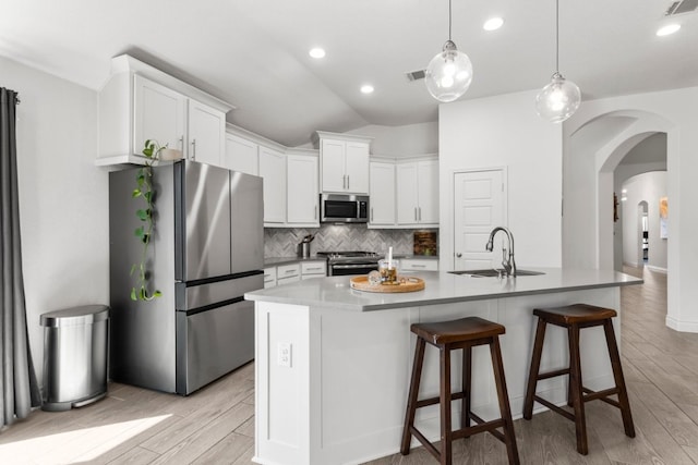 kitchen featuring arched walkways, a sink, appliances with stainless steel finishes, light wood-type flooring, and backsplash