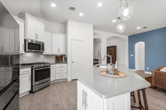 kitchen featuring visible vents, light wood-type flooring, a sink, arched walkways, and appliances with stainless steel finishes