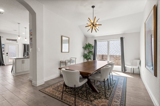 dining space featuring baseboards, light wood-type flooring, vaulted ceiling, an inviting chandelier, and arched walkways