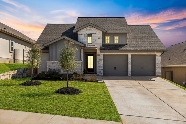 view of front of home with a shingled roof, concrete driveway, a front lawn, stone siding, and board and batten siding