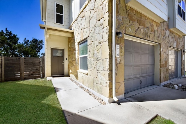 property entrance with a garage, fence, stone siding, and driveway