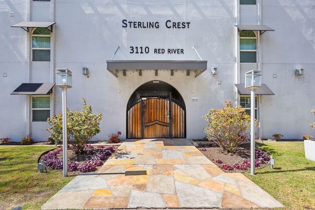 entrance to property featuring stucco siding, a lawn, and a gate