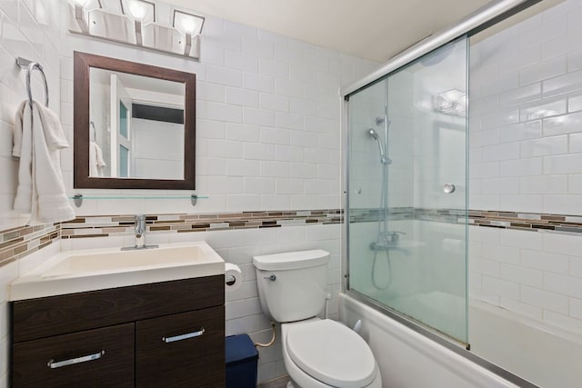 bathroom featuring toilet, vanity, decorative backsplash, shower / bath combination with glass door, and tile walls