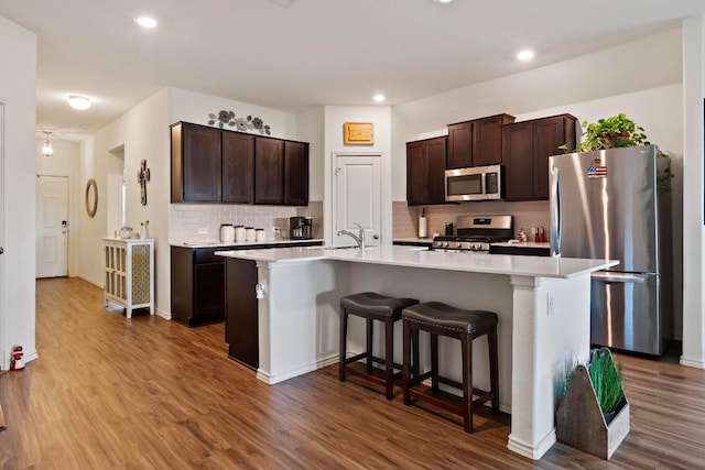 kitchen with dark brown cabinets, appliances with stainless steel finishes, a breakfast bar, and wood finished floors