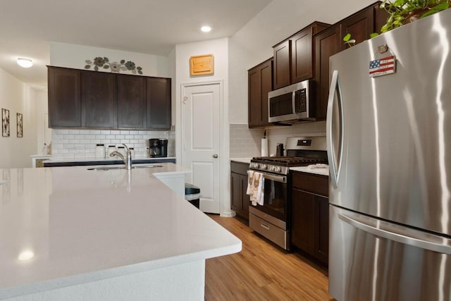 kitchen featuring light wood finished floors, a sink, dark brown cabinetry, light countertops, and appliances with stainless steel finishes