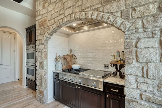 kitchen with backsplash, stainless steel appliances, arched walkways, light wood-style floors, and dark brown cabinets