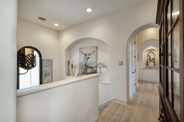 corridor with baseboards, visible vents, light wood-style flooring, recessed lighting, and arched walkways