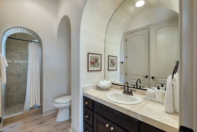 full bathroom with a tile shower, toilet, vanity, and wood finished floors