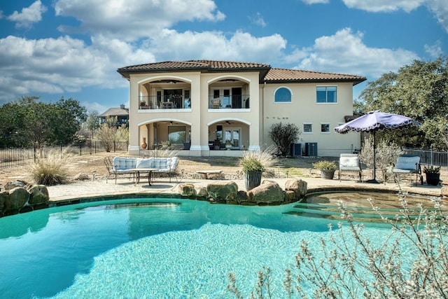 rear view of property with fence, a tiled roof, a balcony, a patio area, and an outdoor pool