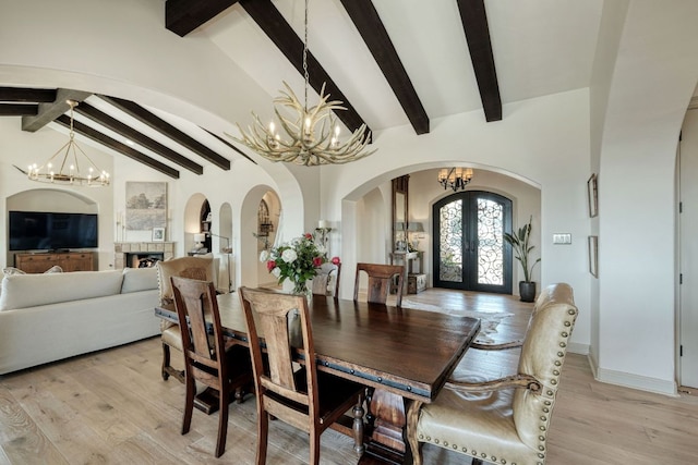 dining room featuring lofted ceiling with beams, french doors, arched walkways, light wood-style floors, and an inviting chandelier