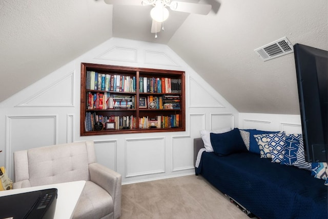 living area featuring carpet, a decorative wall, a ceiling fan, and visible vents