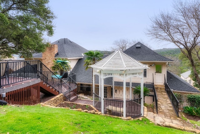 rear view of house with a shingled roof, stairway, a wooden deck, a gazebo, and a lawn