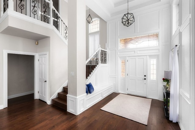 foyer entrance with a decorative wall, stairway, a high ceiling, and dark wood-type flooring