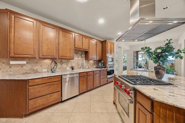 kitchen with brown cabinetry, light tile patterned flooring, decorative backsplash, appliances with stainless steel finishes, and exhaust hood