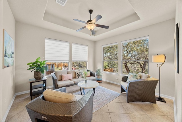 living room featuring light tile patterned flooring, visible vents, a raised ceiling, and a ceiling fan