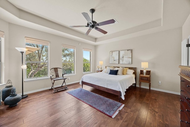 bedroom featuring a tray ceiling, baseboards, hardwood / wood-style floors, and a ceiling fan