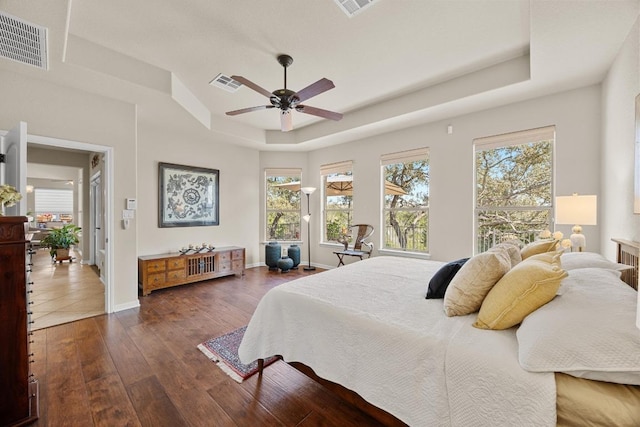 bedroom with visible vents, baseboards, dark wood-type flooring, and a tray ceiling