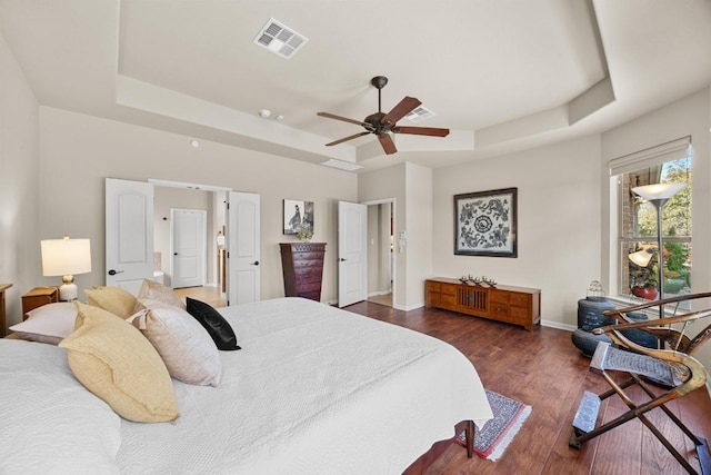 bedroom featuring dark wood finished floors, a tray ceiling, baseboards, and visible vents