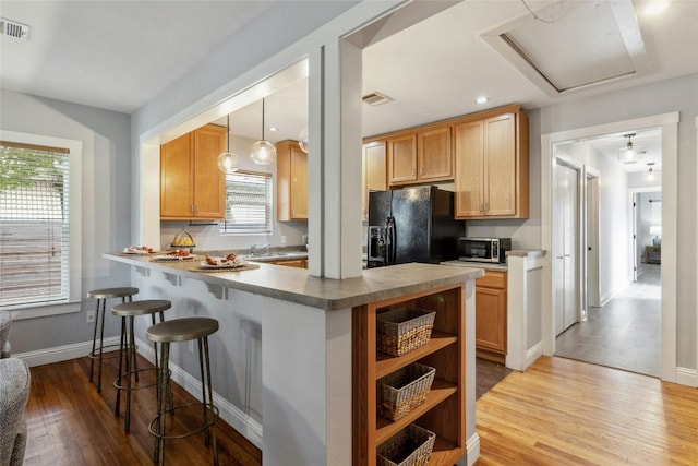 kitchen featuring stainless steel microwave, a kitchen breakfast bar, black fridge with ice dispenser, a peninsula, and light wood finished floors