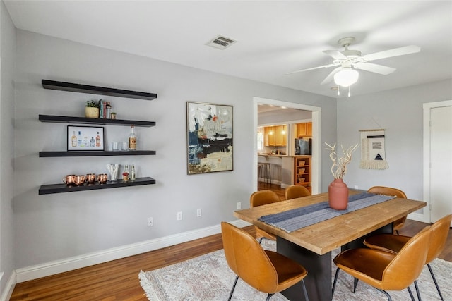 dining space with visible vents, baseboards, a dry bar, wood finished floors, and a ceiling fan