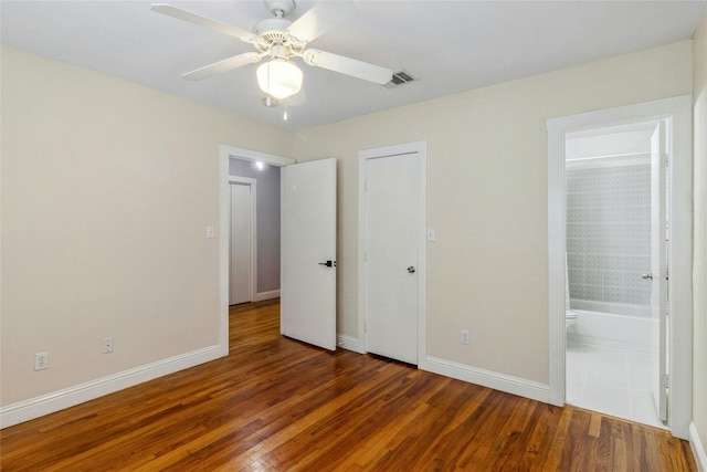 unfurnished bedroom featuring visible vents, baseboards, wood finished floors, and ensuite bathroom