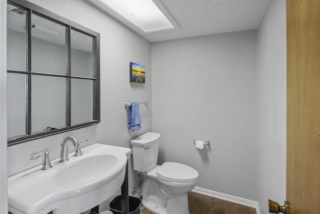 bathroom with toilet, a sink, wood finished floors, baseboards, and a textured wall