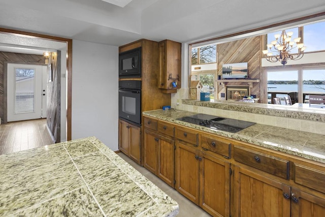 kitchen featuring tile counters, brown cabinets, light wood-style floors, an inviting chandelier, and black appliances