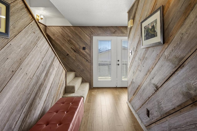 interior space with wooden walls, stairway, french doors, a textured ceiling, and wood-type flooring