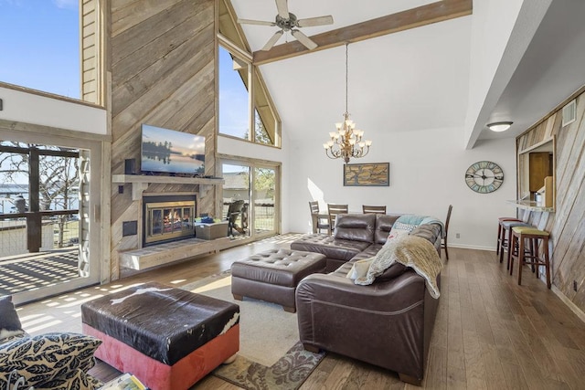 living area with beamed ceiling, hardwood / wood-style floors, ceiling fan with notable chandelier, a fireplace, and high vaulted ceiling