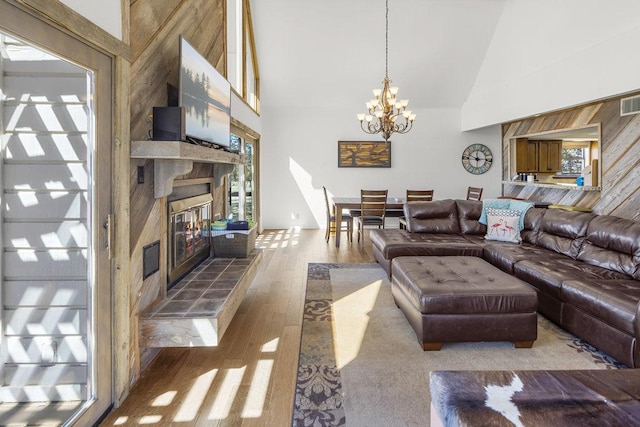 living room with visible vents, a tile fireplace, an inviting chandelier, wood finished floors, and high vaulted ceiling