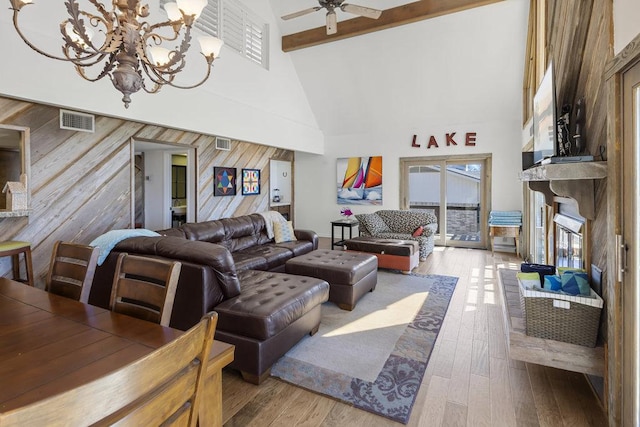 living room featuring visible vents, ceiling fan with notable chandelier, a glass covered fireplace, wood-type flooring, and a high ceiling