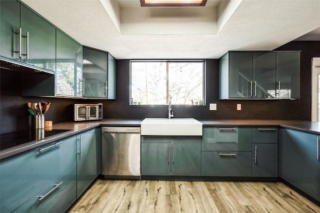 kitchen with stainless steel dishwasher, dark countertops, green cabinets, and a sink