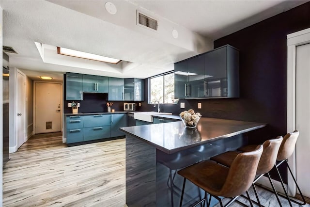 kitchen featuring visible vents, a kitchen bar, dark countertops, a peninsula, and light wood finished floors