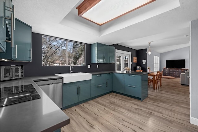 kitchen featuring light wood-type flooring, a sink, a tray ceiling, stainless steel dishwasher, and a peninsula