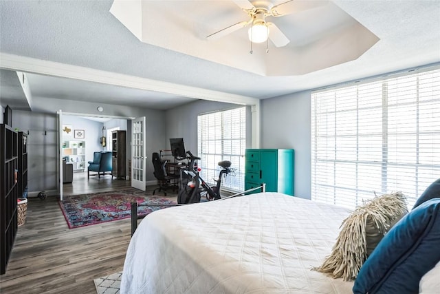 bedroom featuring wood finished floors, baseboards, ceiling fan, a textured ceiling, and a raised ceiling