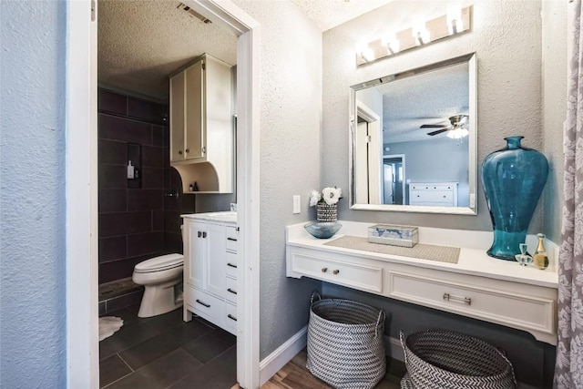 full bath with vanity, a ceiling fan, visible vents, a textured ceiling, and a textured wall