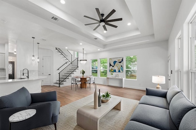 living room with visible vents, stairway, wood finished floors, a raised ceiling, and a ceiling fan