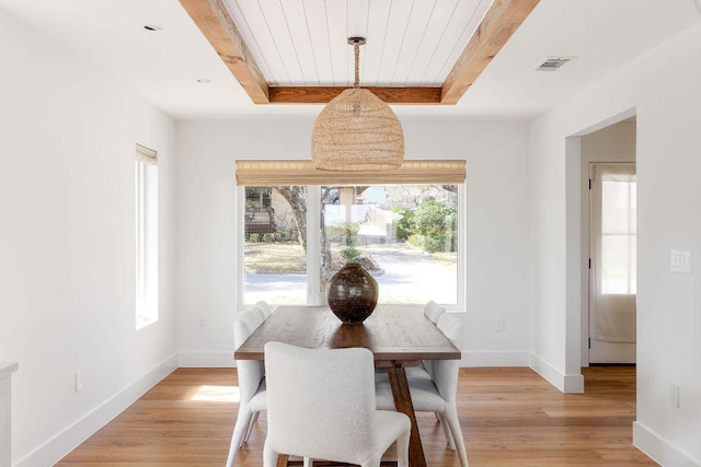 dining area featuring visible vents, baseboards, light wood-style floors, and a raised ceiling