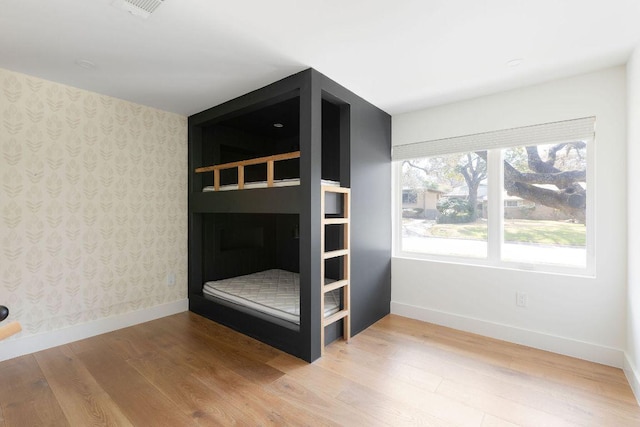 unfurnished bedroom with visible vents, wallpapered walls, baseboards, and wood finished floors