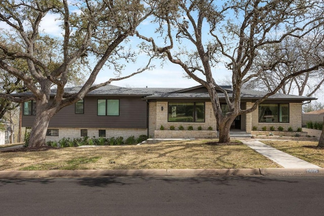 view of front of property featuring stone siding, a front lawn, and a shingled roof