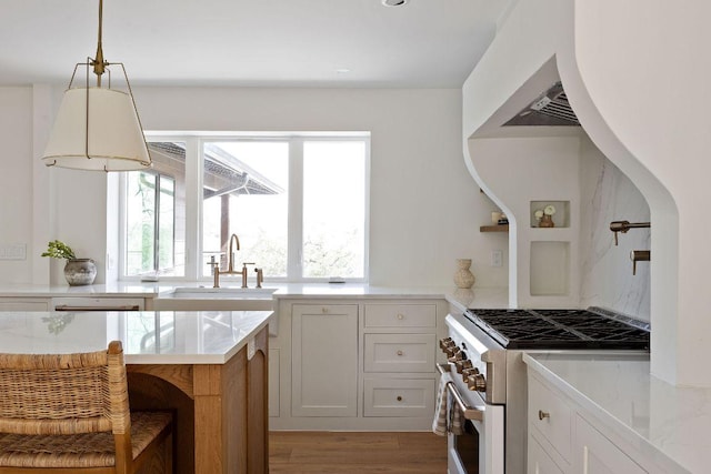 kitchen with light wood-style flooring, stainless steel range, a sink, light countertops, and hanging light fixtures