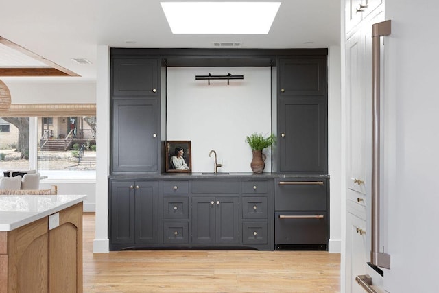 bar featuring visible vents, a skylight, light wood-style floors, a warming drawer, and a sink