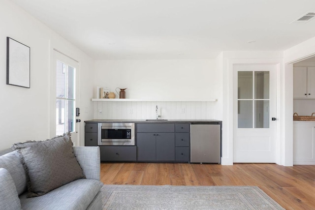 interior space with stainless steel microwave, gray cabinets, light wood finished floors, and a sink