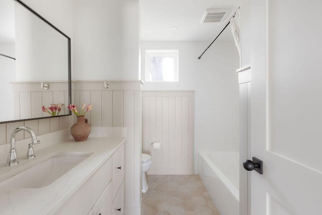 bathroom featuring vanity, washtub / shower combination, visible vents, wainscoting, and toilet